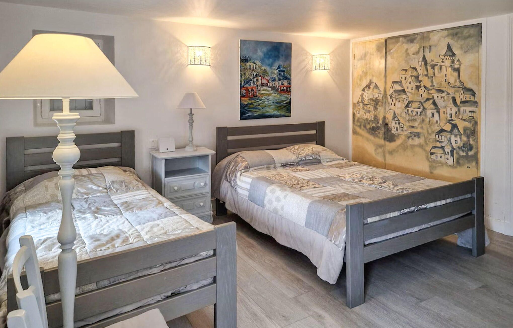 A bedroom with two beds, nightstands, a lamp, and wall art.
