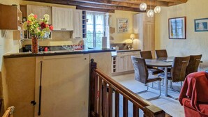 A kitchen with a dining area, wooden beams, and a staircase. - Charmante maison avec piscine (Castelnaud-la-Chapelle)