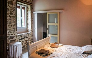Ein Schlafzimmer mit Steinsturz, Fenster, Bett mit weißer Bettdecke und Holzschrank mit Milchglas-Türen.