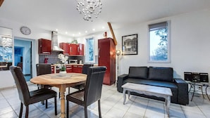 Eine moderne Küche mit roten Schränken, einem Esstisch mit Stühlen, einem schwarzen Sofa und einem kleinen Tisch mit einer Lampe.