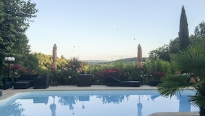Ein Schwimmbad mit umgebender Bepflanzung und Blick auf die Landschaft, sowie zwei Sonnenschirme.