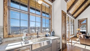 A kitchen with a large window, wooden beams, stainless steel appliances, and a coffee maker on the counter. - Sundance Lodge at Eagles Nest - hot tub, mtn home, club amenities (Elk Park)