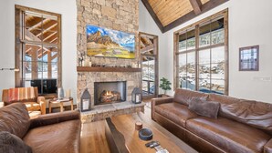 A spacious living room with a stone fireplace, leather sofas, and large windows. - Sundance Lodge at Eagles Nest - hot tub, mtn home, club amenities (Elk Park)