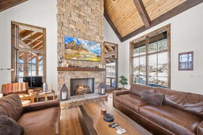 Ein großzügiges Wohnzimmer mit Kamin aus Stein, Ledersofas und großen Fenstern.