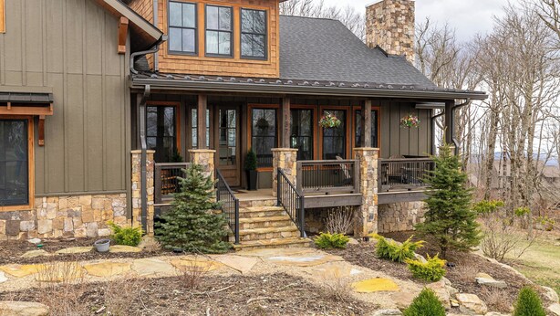 A two-story house with a stone chimney, a porch with a railing, and a small staircase leading to the entrance. - The Sugar Chalet - Luxury home on Sugar, easy access, views! (Sugar Mountain)