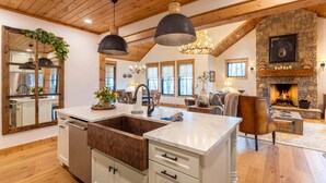 A spacious kitchen with a large island, wooden ceiling beams, and a stone fireplace. - The Sugar Chalet - Luxury home on Sugar, easy access, views! (Sugar Mountain)