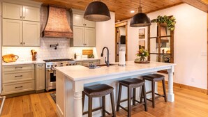 A kitchen with wooden ceiling, white cabinets, a large island with stools, and pendant lighting. - The Sugar Chalet - Luxury home on Sugar, easy access, views! (Sugar Mountain)