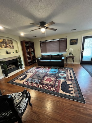 A living room with a fireplace, a sofa, a patterned rug, and a ceiling fan. - Spacious DIA House 3BR + Bonus Bed House (Denver)