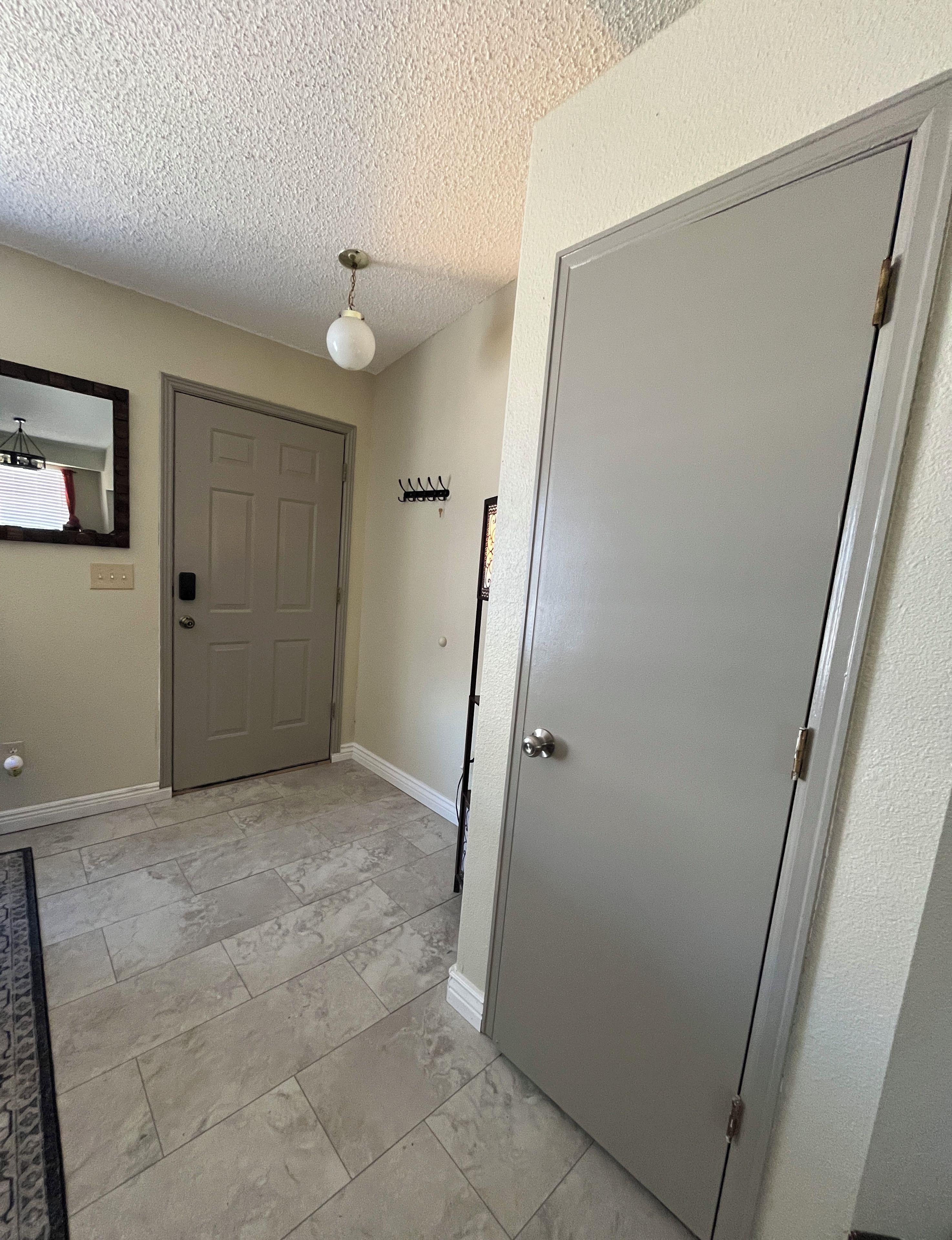 A hallway with a closed door, a coat rack, and a ceiling light fixture.