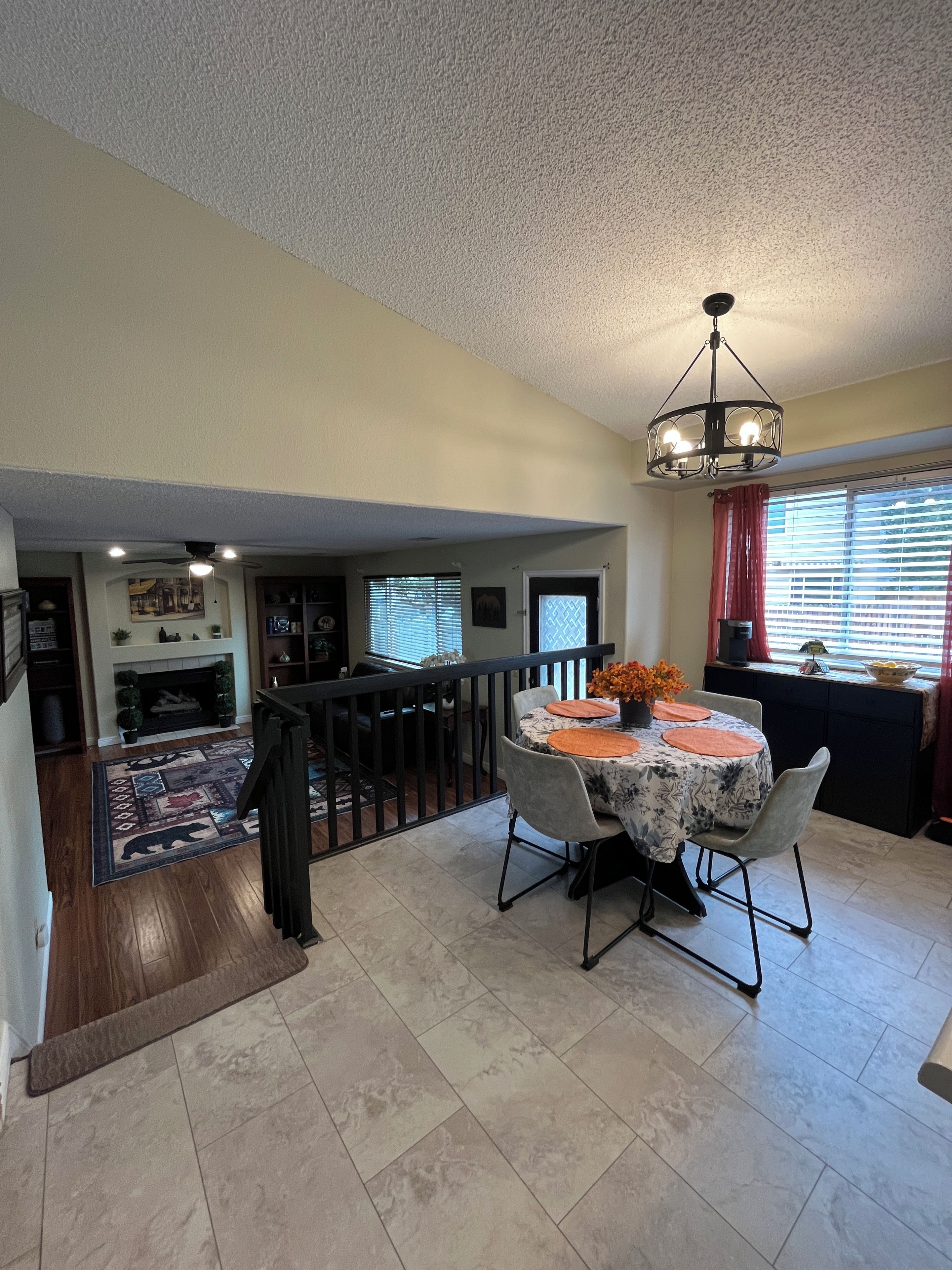 A dining area with a round table, chairs, and a chandelier. There is a staircase leading to an upper level.