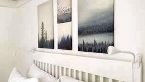 A bedroom with a white headboard, a bed with white bedding, and three framed landscape paintings on the wall. - 1740 Le Cocon Limoilou Enfant-Jésus Hospital (Québec)