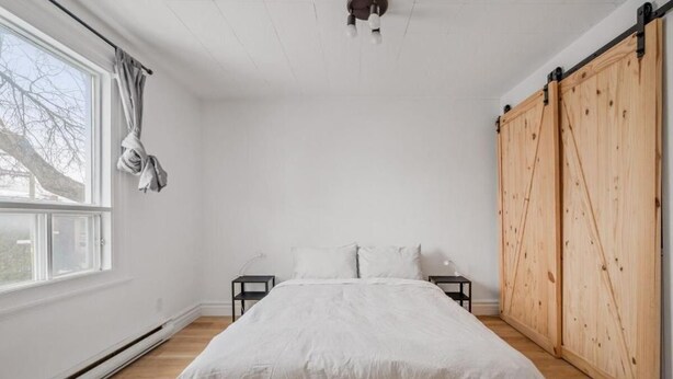 A bedroom with a bed, a window, a sliding door, and a nightstand. - Le Petit Cozy, 1 CH, Office, Enfant-Jésus (Québec)