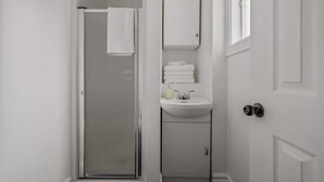 A bathroom with a glass shower door, a white sink, a mirror, and a cabinet. - Le Petit Cozy, 1 CH, Office, Enfant-Jésus (Québec)