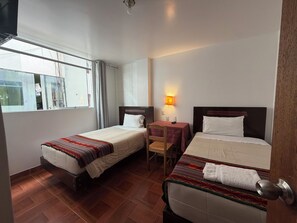 A hotel room with two beds, a small table, a chair, a window, and a wall-mounted lamp. - Machu Picchu Sacred Valley (Aguas Calientes)