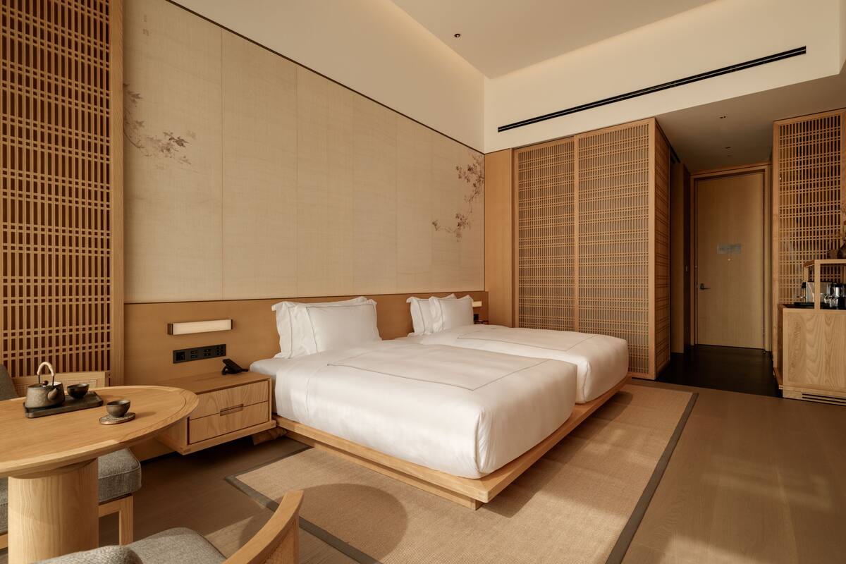 A modern hotel room with a large bed, a small table with tea set, and a traditional sliding door.