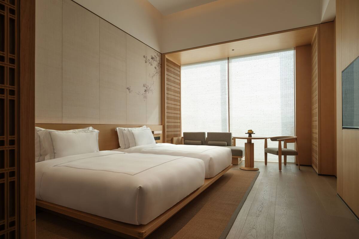 A hotel room with two beds, a small table, and a chair.