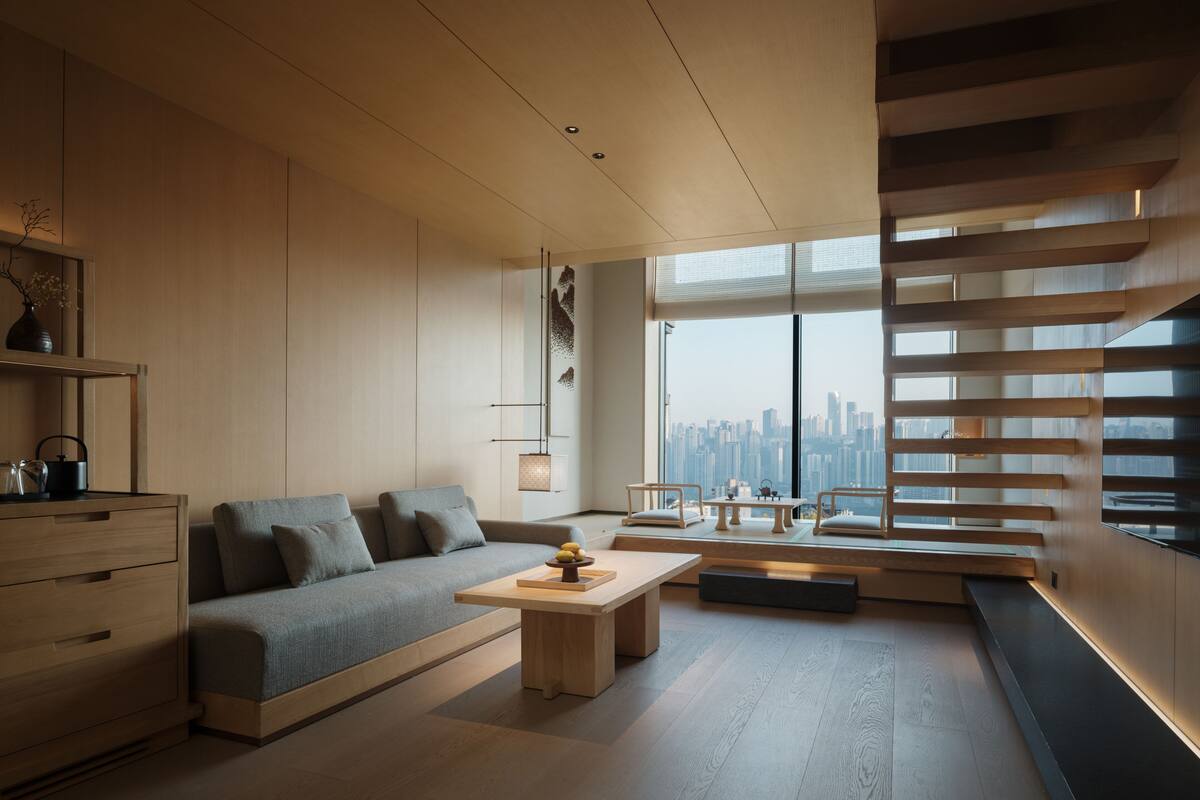 A modern living room with a sofa, coffee table, and a city view through large windows.