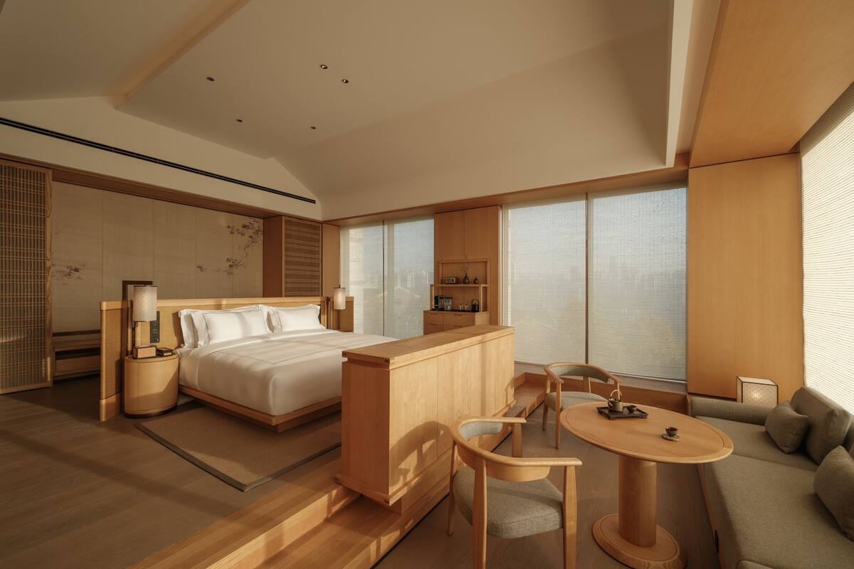A modern hotel room with a bed, a wooden desk, a sofa, and a dining table.