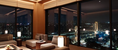 Una habitación de hotel moderna con ventanas amplias, vistas a la ciudad y una zona de estar acogedora.