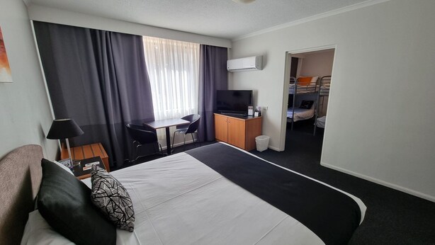 A hotel room with a bed, desk, chair, TV, and a bunk bed in the adjacent room. - Alpha Hotel Canberra (Canberra)