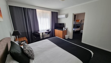 Habitación de hotel con cama, escritorio, silla, televisión y literas en la habitación contigua.