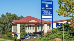 A hotel with a red roof, a blue signboard listing amenities like Wi-Fi, a restaurant, and a gym. - Alpha Hotel Canberra (Canberra)