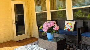Eine überdachte Veranda mit Deckenventilator, Korbmöbeln, einem Blumentopf und einem gemusterten Teppich.