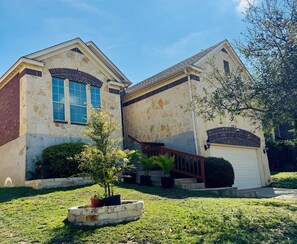 A two-story house with a stone facade, a garage, and a small front yard with a tree and potted plants.