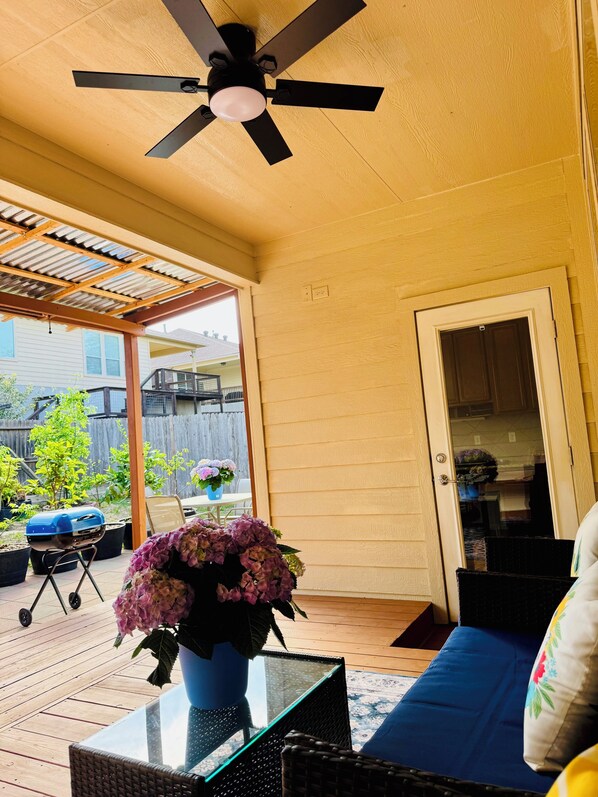 A covered patio area with a ceiling fan, a glass table, wicker furniture, and a door leading to a backyard.