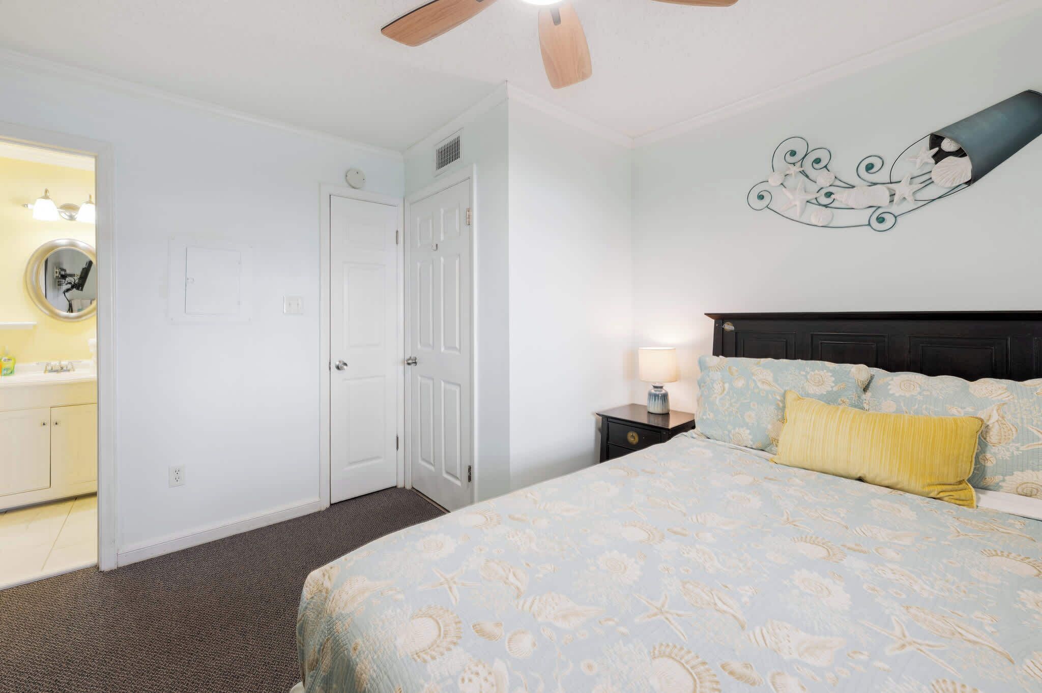 Ein Schlafzimmer mit Bett, Nachttisch, Wanduhr, Deckenventilator und einer Tür.