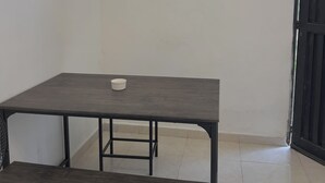 Huoneessa on tumma puinen pöytä ja penkki, pöydällä on valkoinen astia ja seinällä värikäs abstrakti maalaus.