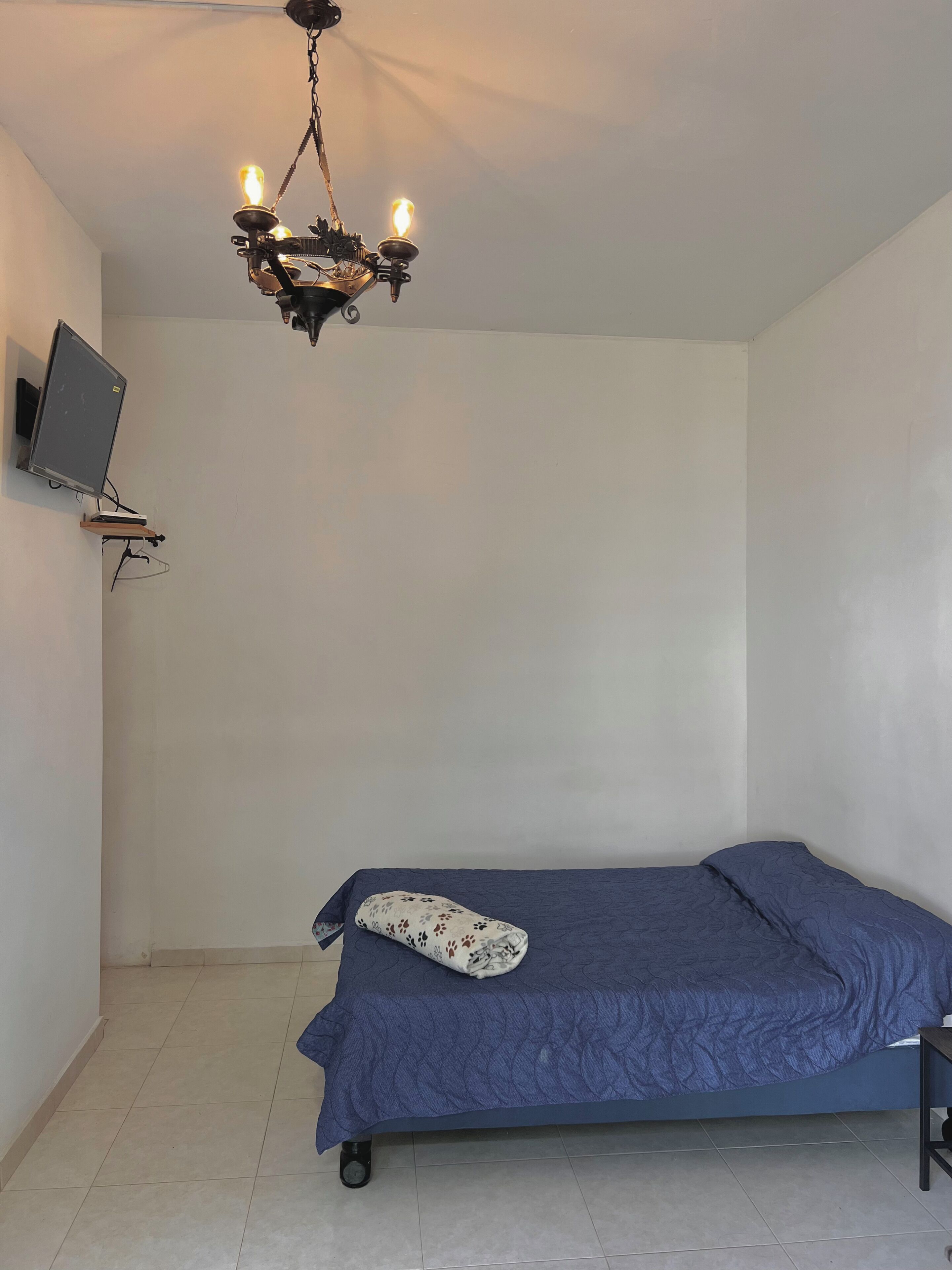 Een slaapkamer met een bed, een plafondlamp, een wandtelevisie en een betegelde vloer.