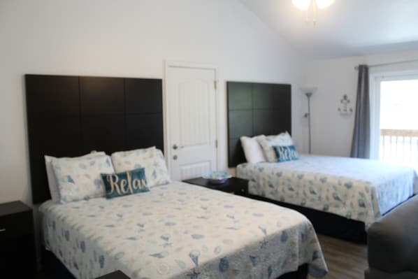 Habitación de hotel con dos camas, una puerta, una mesita de noche y un ventanal.