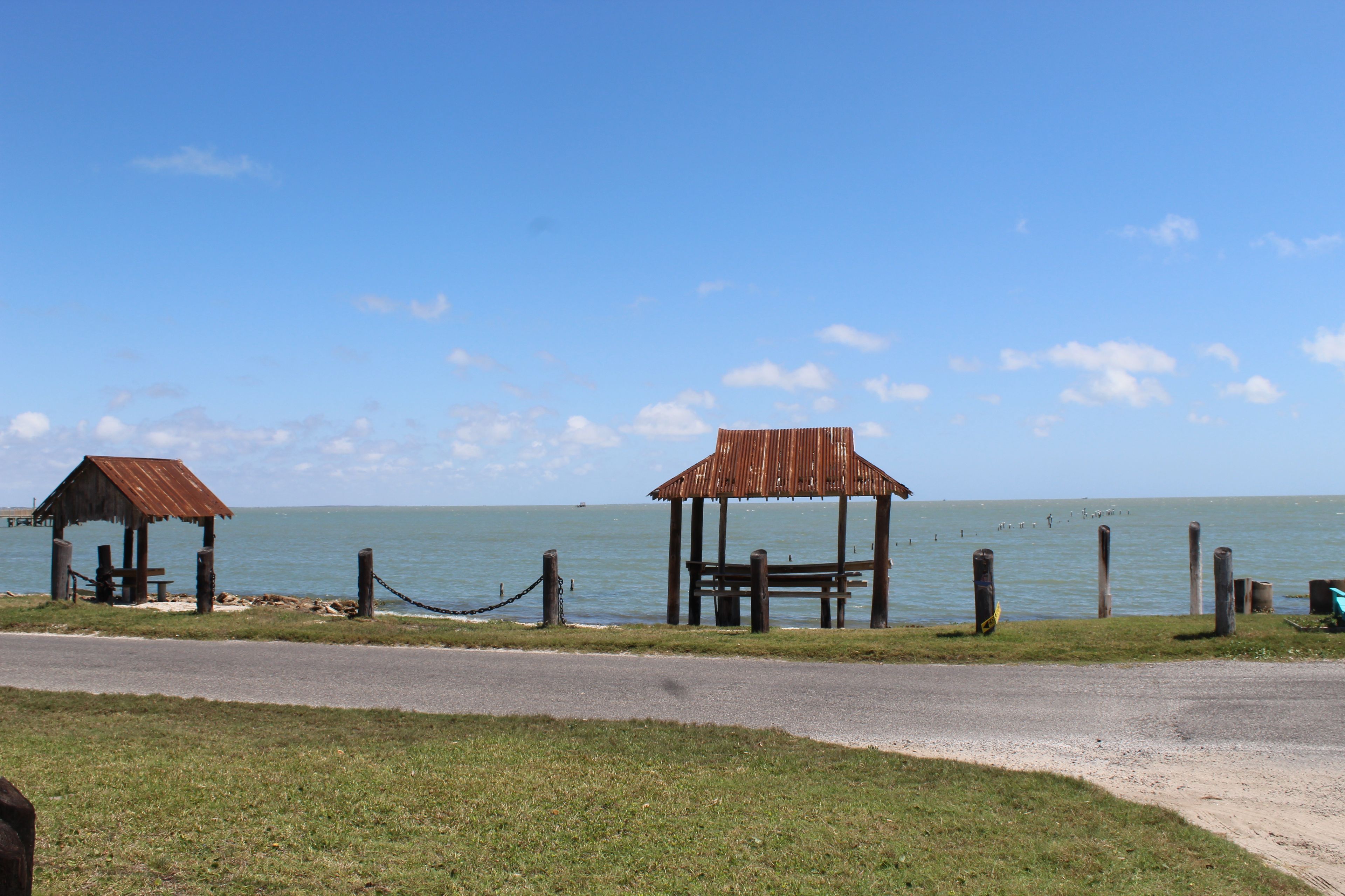 A coastal area with two wooden gazebos and a chain-link fence along the shore.