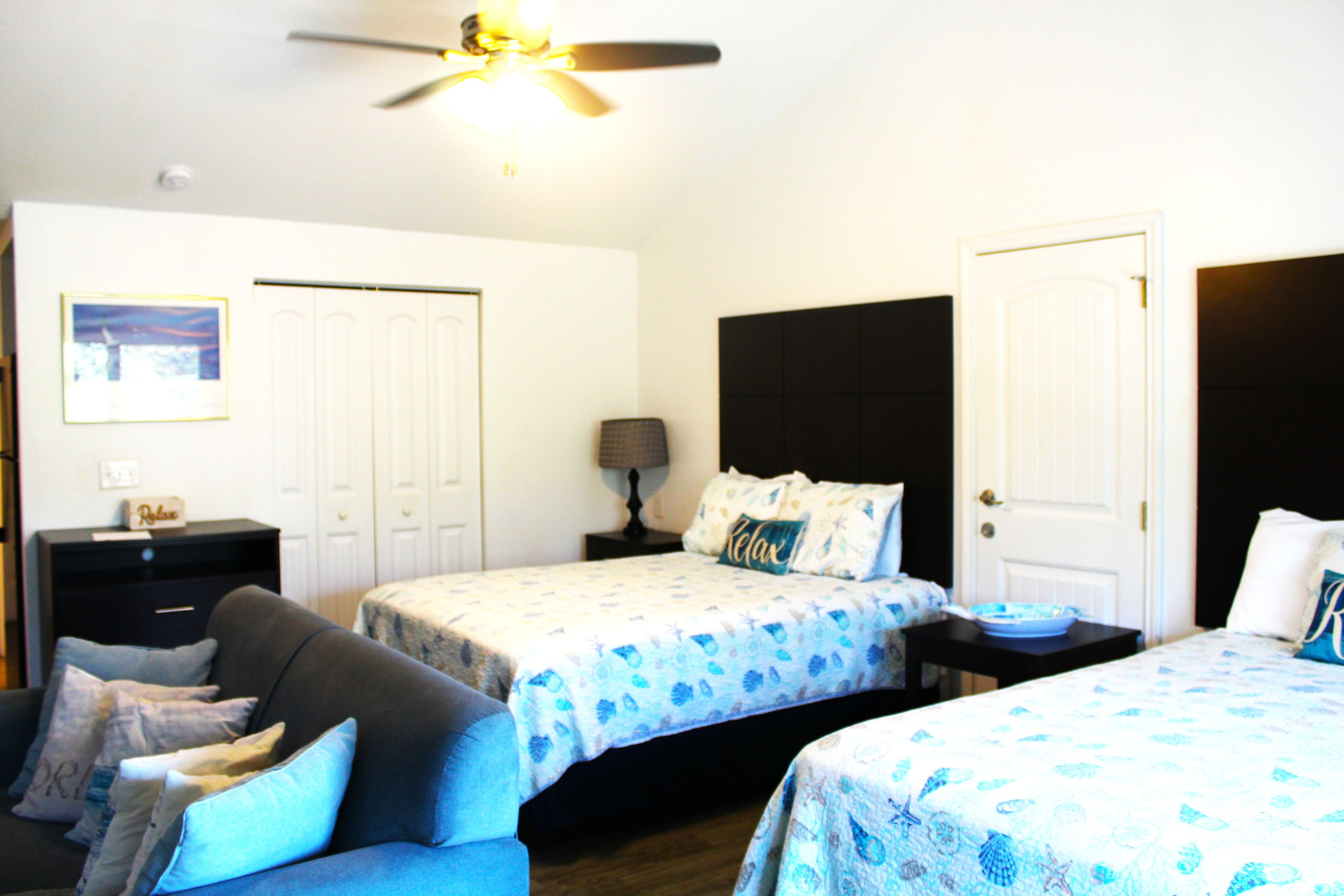 A bedroom with two beds, a ceiling fan, a nightstand, a dresser, and a framed picture on the wall.