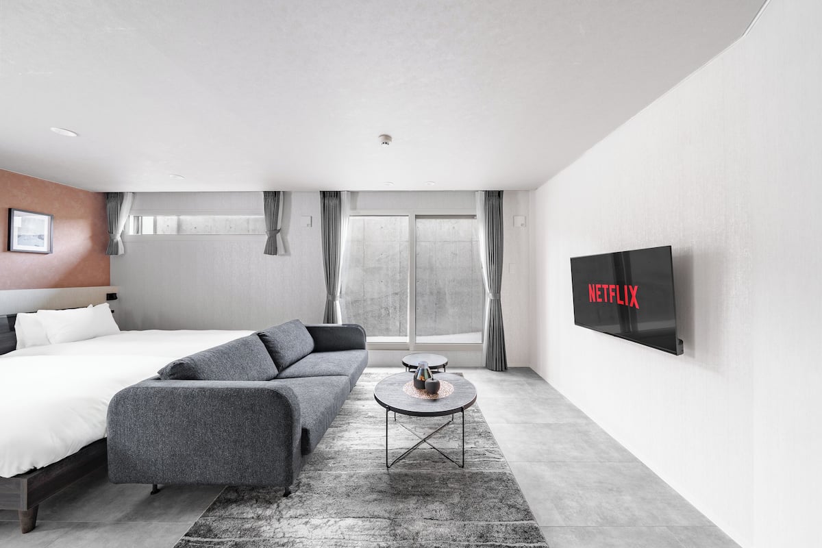 Ein modernes Hotelzimmer mit Bett, Sofa, Couchtisch und einem Fernseher, der 'NETFLIX' zeigt.