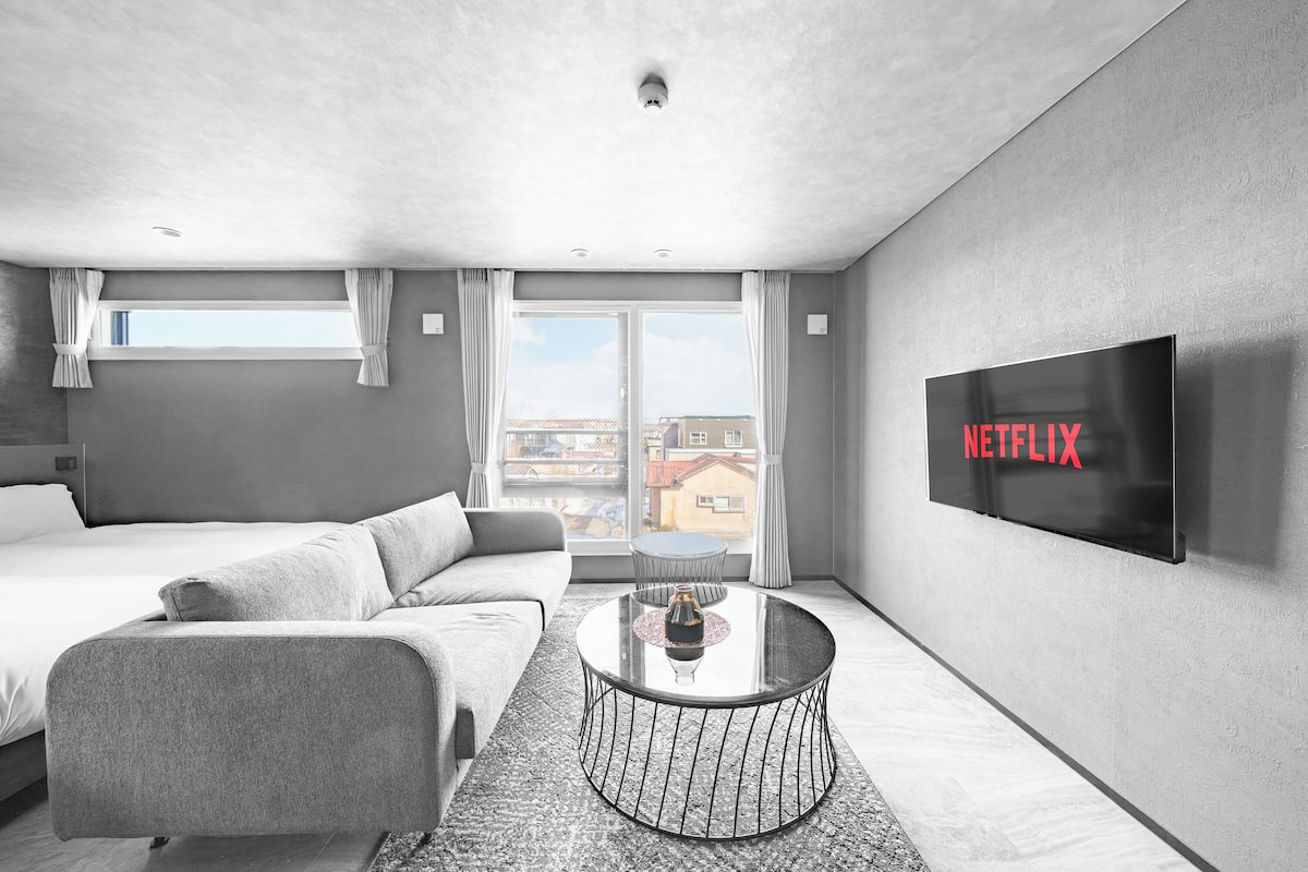 Ein modernes Hotelzimmer mit Bett, Sofa, rundem Couchtisch und einem an der Wand montierten Fernseher.