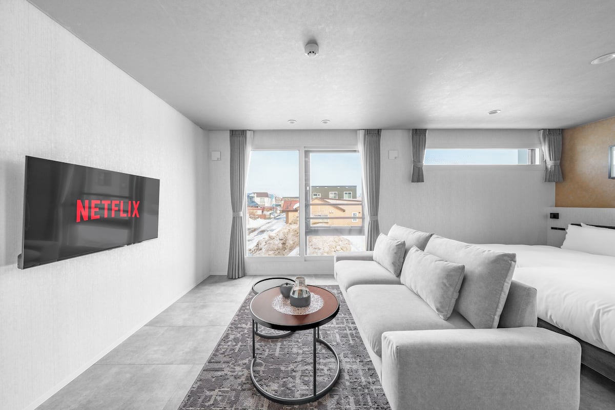 Ein modernes Hotelzimmer mit großem Flachbildfernseher, einer Couch, einem Bett und Blick nach außen.
