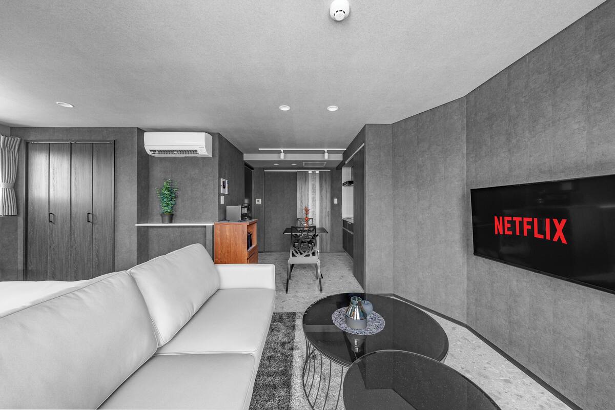Ein modernes Wohnzimmer mit einem weißen Sofa, einem schwarzen Couchtisch und einem Fernseher, der 'NETFLIX' anzeigt.