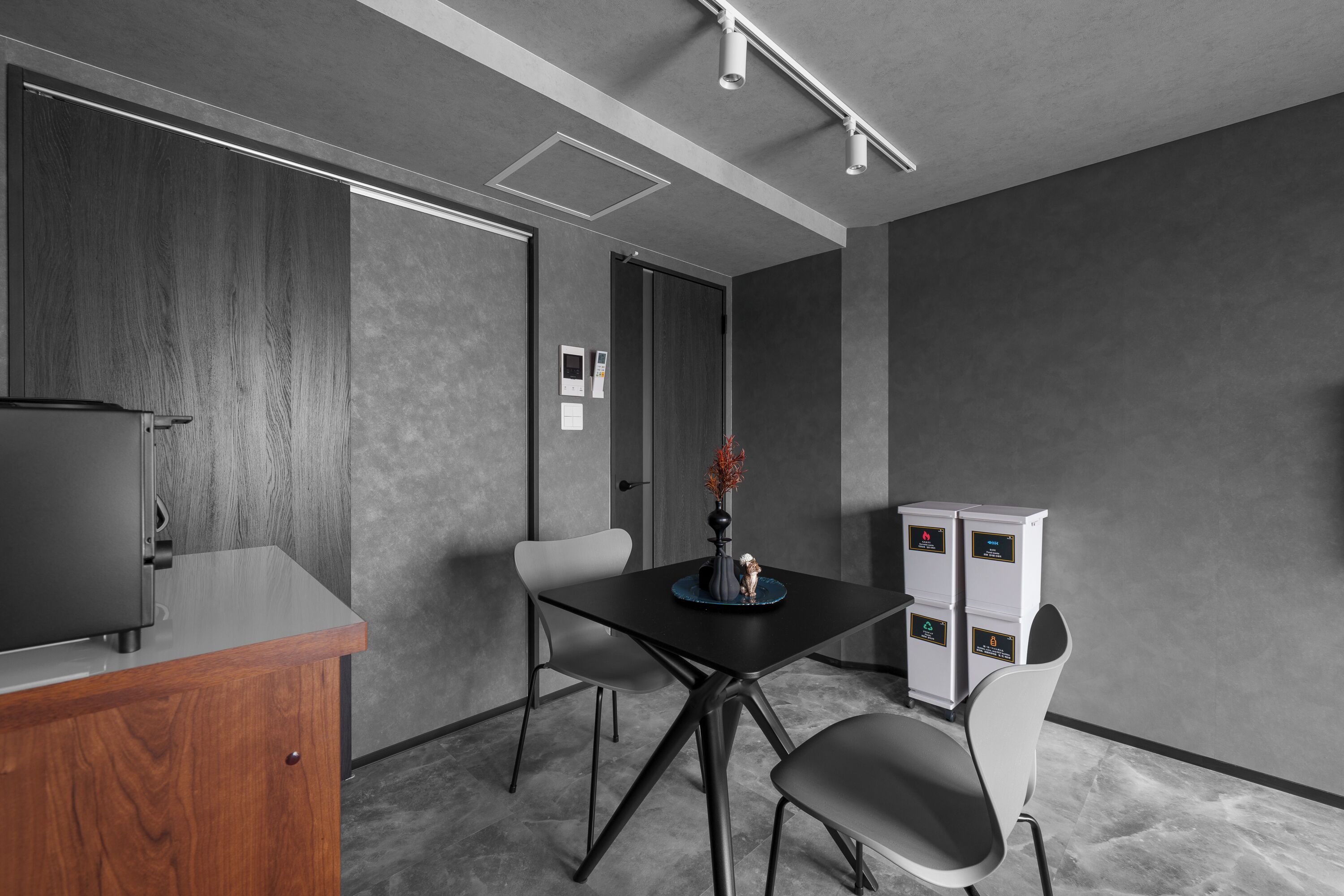 A modern conference room with a wooden cabinet, a black table, and grey chairs.