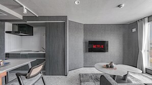 A modern kitchen with a built-in oven, a dining area with a table and chairs, and a living area with a TV mounted on the wall. - GRAN HILLS (Chitose)