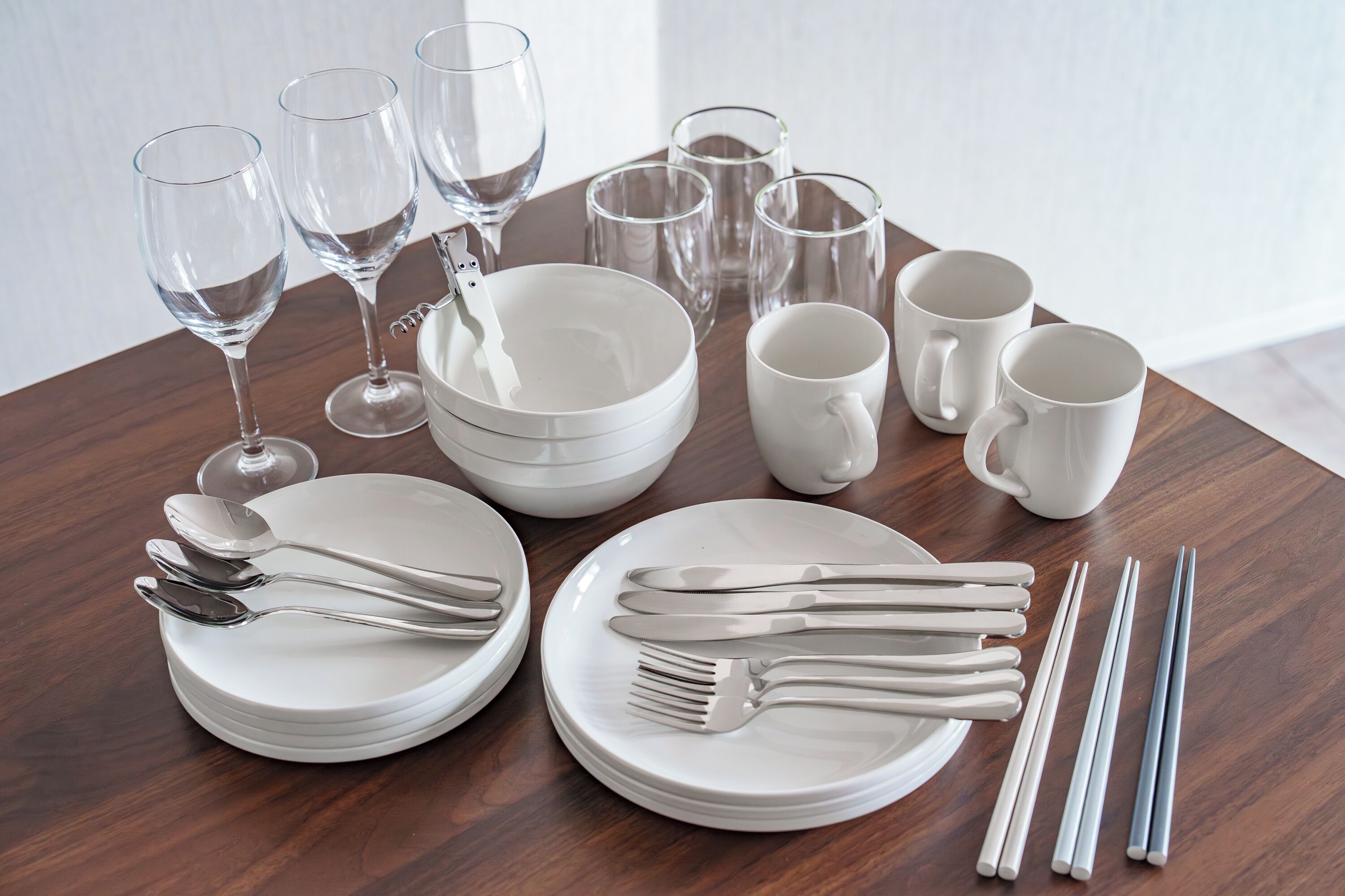 A dining table set with white plates, bowls, glasses, and cutlery.