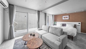 A modern hotel room with a sofa, a bed, a small wooden table, and a large window. - GRAN HILLS (Chitose)