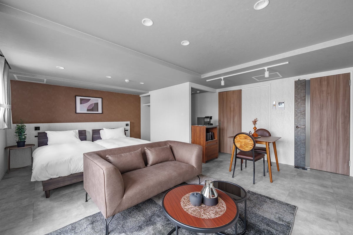 Ein modernes Hotelzimmer mit Bett, Sofa, Esstisch und einer kleinen Küchenzeile.