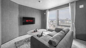 A modern living room with a grey sofa, a round coffee table, and a flat-screen TV mounted on the wall. - GRAN HILLS (Chitose)