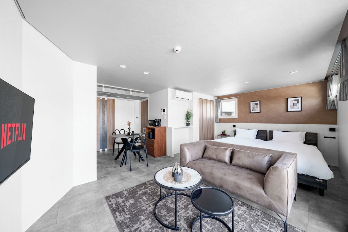 Ein modernes Hotelzimmer mit Bett, einer Couch, einem Essbereich und einem Fernseher, der 'NETFLIX' anzeigt.