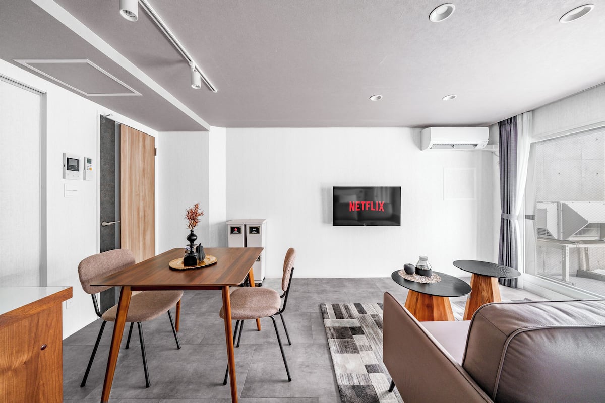 Ein modernes Wohnzimmer mit Essbereich, einer Couch, einem Fernseher, der 'NETFLIX' anzeigt, und einem Fenster mit Vorhängen.
