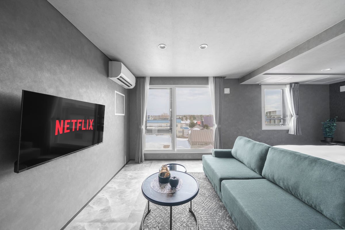 Ein modernes Hotelzimmer mit großem Flachbildfernseher, einer Couch, einem kleinen runden Tisch und einem Balkon mit Aussicht.