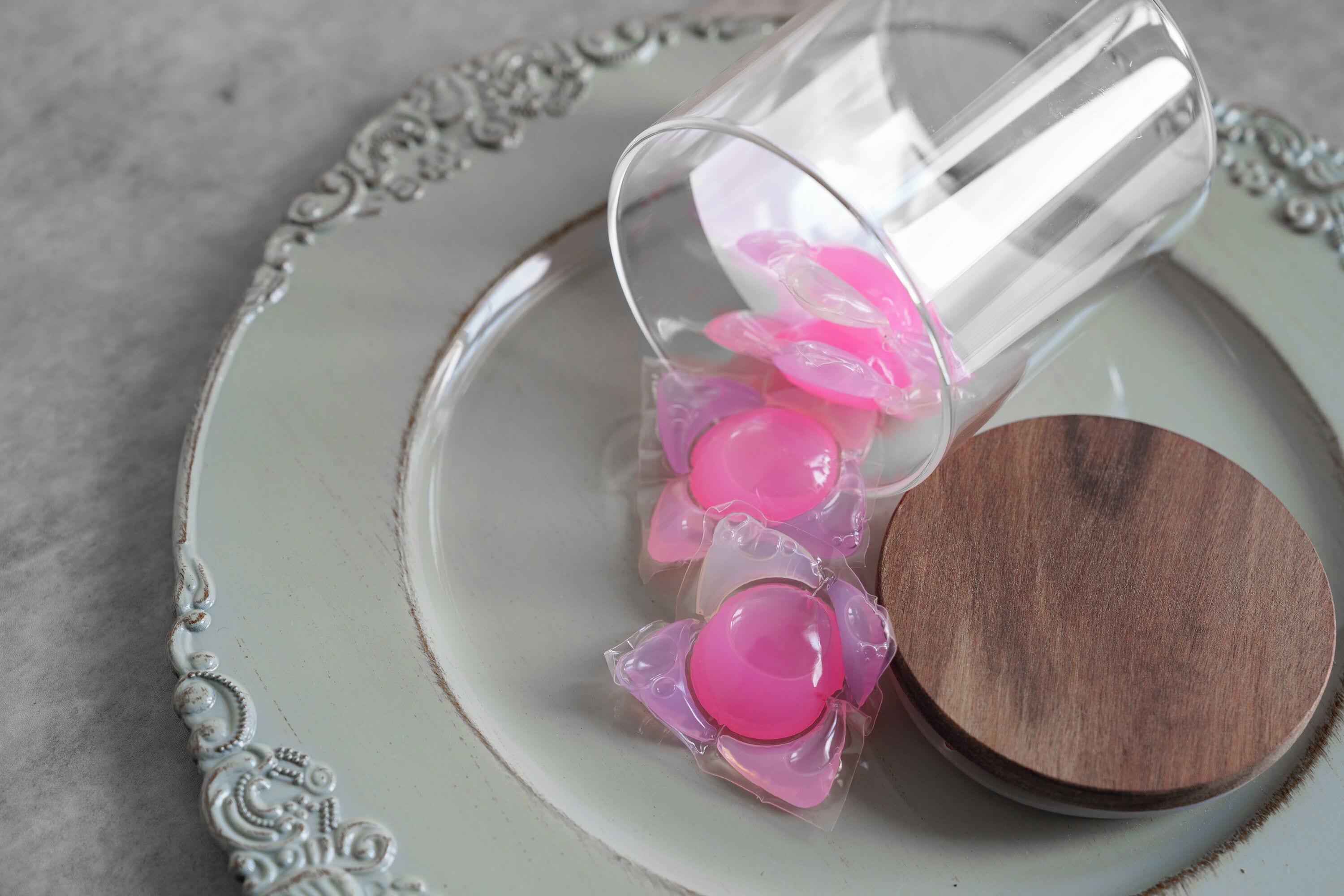 Een glazen fles met roze inhoud op een keramieken bord met houten deksel.