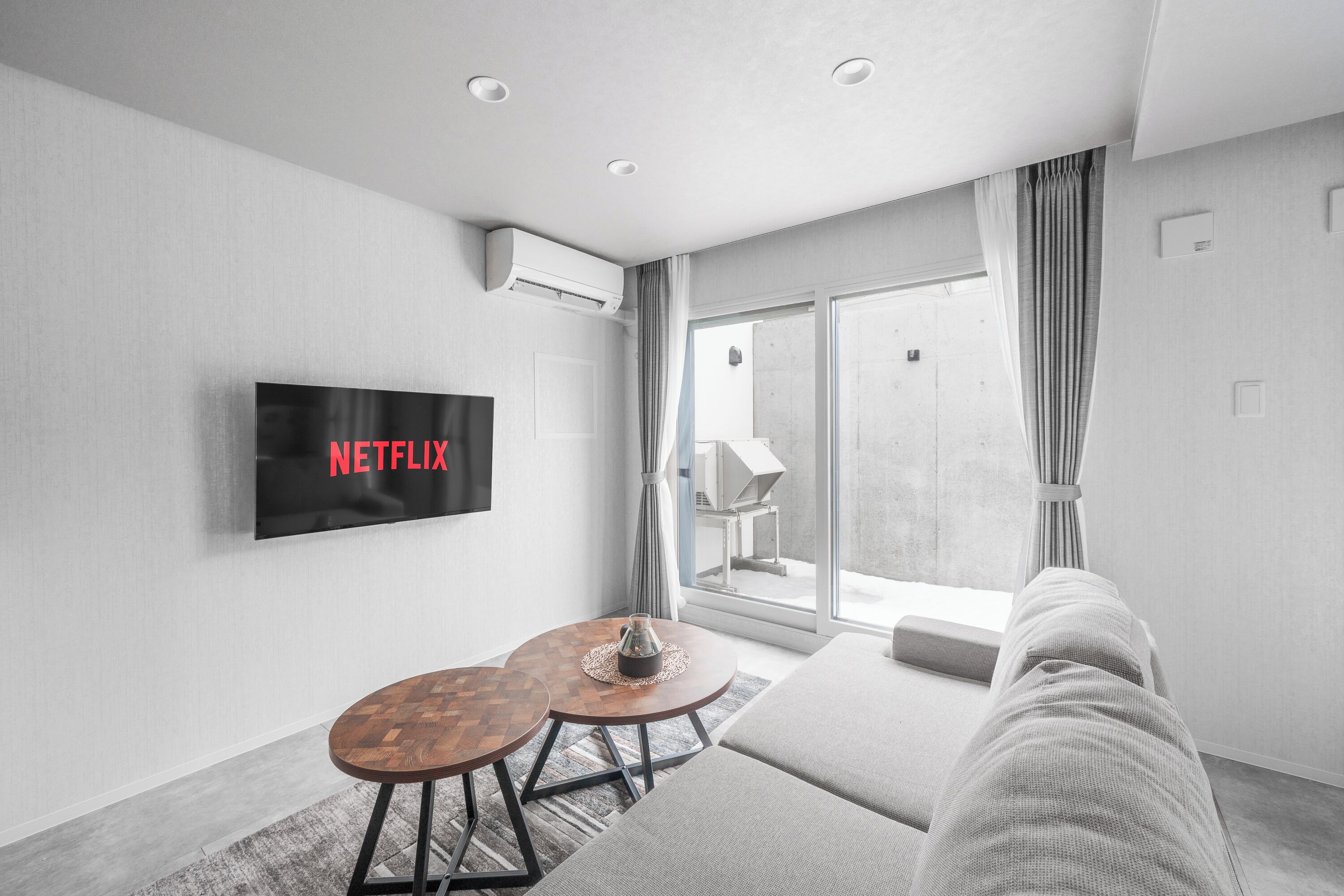 A modern living room with a flat-screen TV, a sofa, a coffee table, and a large window.
